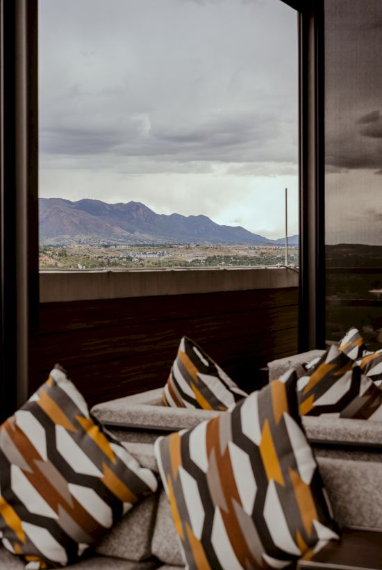 A cocktail in a martini glass, garnished with a twist of orange peel, set against a blurred, dimly lit bar background.