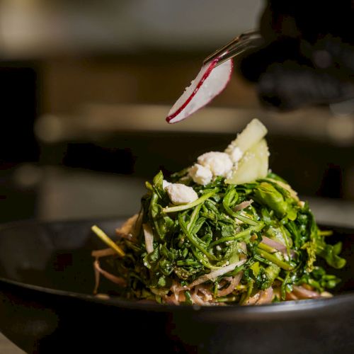 A fork holds a bite of leafy salad over a plate, with greens, onions, and cheese.