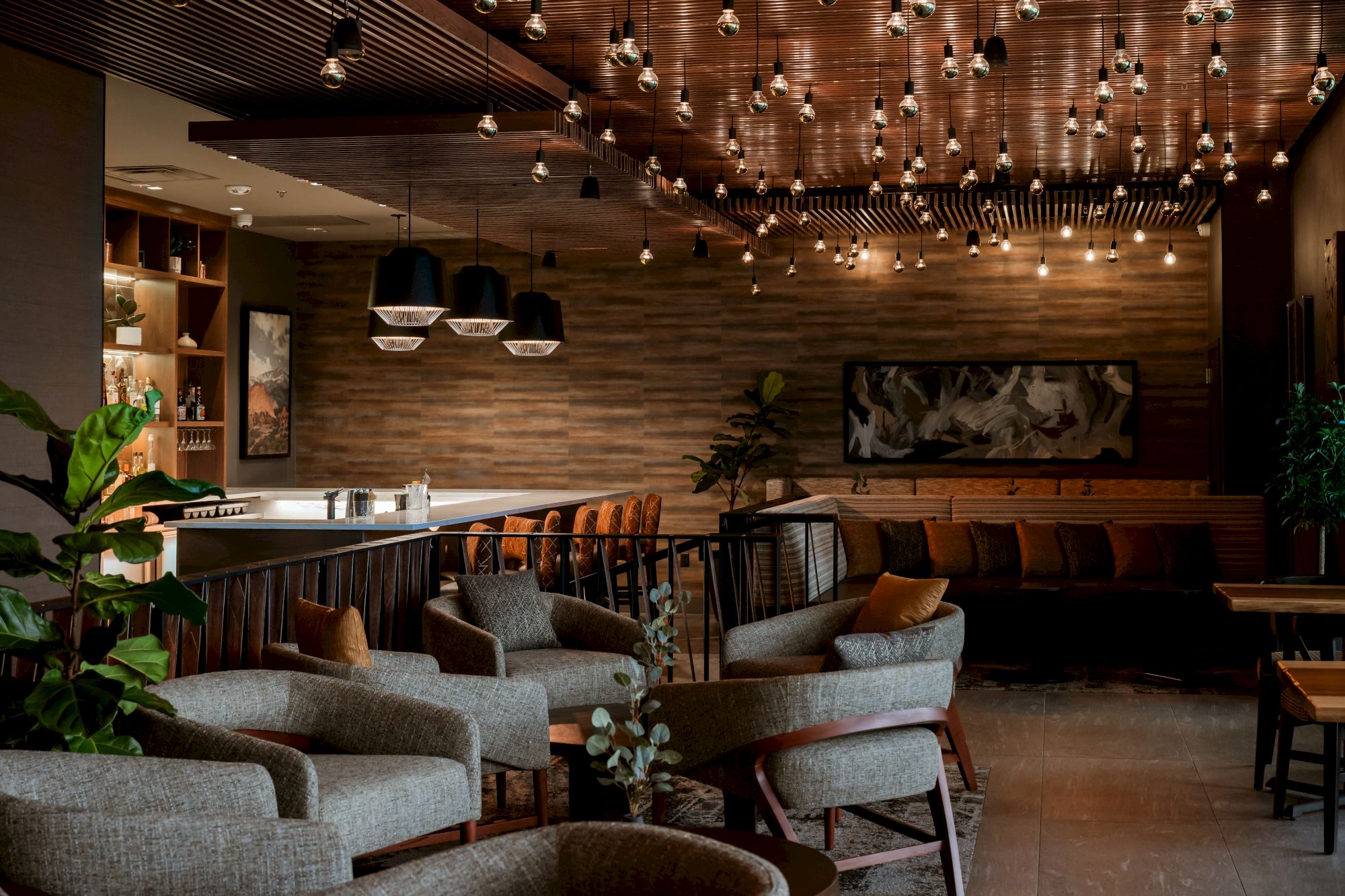 An upscale lounge bar interior with wood walls, hanging globe lights, a counter, and cozy seating and plants.