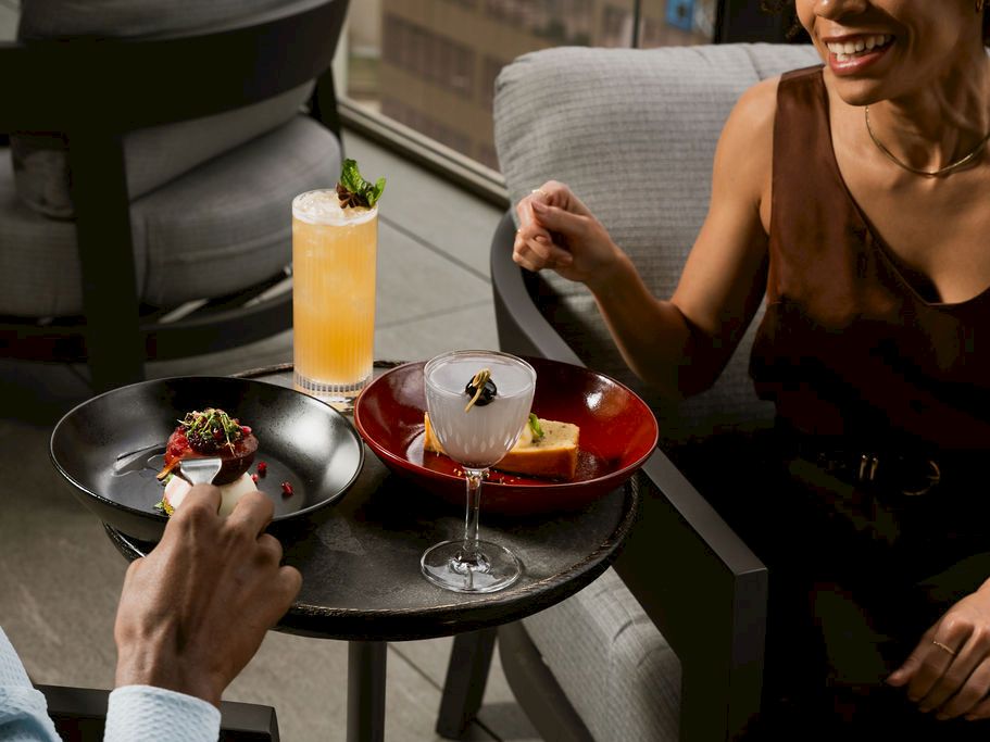 An outdoor restaurant table with colorful cocktails and plated appetizers as people clink and laugh in the sun.